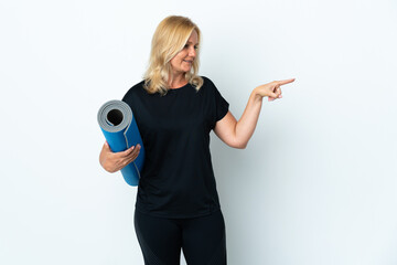 Wall Mural - Middle age woman going to yoga classes while holding a mat isolated on white background pointing to the side to present a product