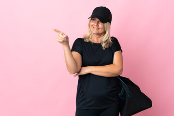 Canvas Print - Middle age woman with sport bag isolated on pink background pointing finger to the side