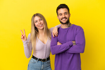 Wall Mural - Young couple over isolated yellow background smiling and showing victory sign