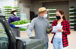 © JackF - Young girl buyer in face mask discussing delivery of seedlings with man worker at greenhouse