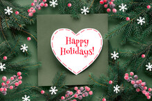 Green Red Christmas Background With Text Happy Holidays On White Paper Heart Shape. Natural Xmas Twigs Decorated With Frosted Berries And Paper Snowflakes. Flat Lay, Top View On Dark Green Paper.