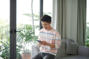 Young man sitting relaxed on sofa with laptop checking his smartphone messages