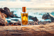 A golden transparent perfume bottle with drops on a sea log. Close-up. In the background, the ocean. Concept of International Fragrance Day
