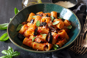 Pasta alla norma - Italian pasta with eggplante, tomato sauce and parmesan cheese on dark table. Top view. Healthy food.