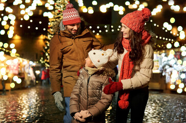 Canvas Print - family, winter holidays and celebration concept - happy mother, father and little daughter at christmas market on town hall square in tallinn, estonia