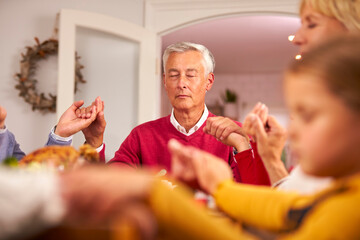 Wall Mural - Multi Generation Family Hold Hands Around Table At Home Saying Grace Before Eating Christmas Meal