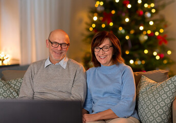 Wall Mural - winter holidays, leisure and people concept - happy smiling senior couple watching tv at home in evening over christmas tree lights on background