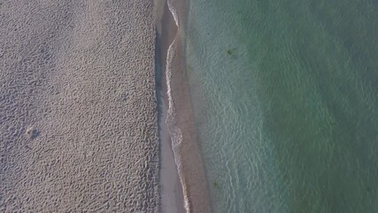 Wall Mural - Aerial drone view of a beautiful beach and sea water on sunrise with man walking on the beach