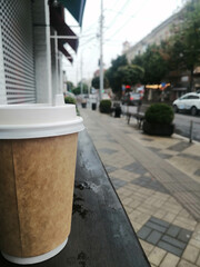 Sticker - Vertical shot of a brown coffee takeaway cup on a wooden platform in the street on a rainy day