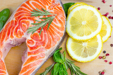 Wall Mural - Top view of raw red salmon fish slices with herbs, spices and lemon in the kitchen on light wooden background ready for cooking.