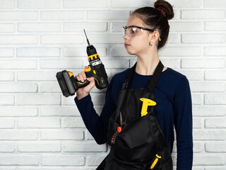 A young girl works with a drill. Working environment in a carpentry workshop. Cordless cordless drill - screwdriver with drill. Construction tools set. Professional repair equipment.