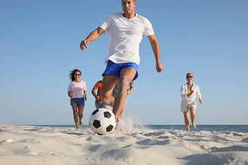 Poster - Group of friends playing football at beach, focus on ball