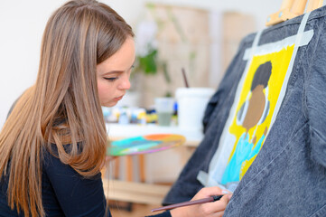 Young woman with brush drawing on a jeans. Stylish individual clothes by a professional artist