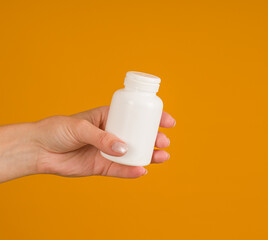 hand holds white bottle for pills on yellow background, close-up