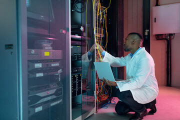African american male computer technician using laptop working in business server room
