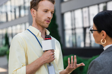 Wall Mural - reporter with microphone talking with asian businesswoman in glasses outside