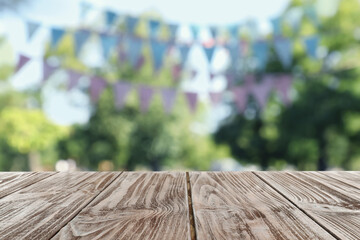 Empty wooden table in park decorated with bunting flags, space for design. Outdoor party