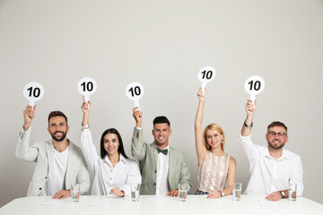 Wall Mural - Panel of judges holding signs with highest score at table on beige background