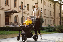Happy Mother Walking With Her Son In Stroller Outdoors