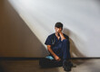 © Cavan Images - Exhausted doctor wearing scrubs sitting on floor in a patch of light.