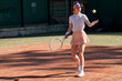 © Roman - Young redhead fit female in stylish white tennis uniform playing tennis, hits the ball with racket. Outdoor on sport court. Youth, flexibility, power and energy. People lifestyle, sport concept