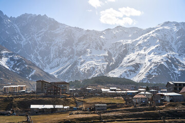 Wall Mural - Early spring. The village is in the mountains. Snow caps on the tops of the mountains. Small village at the foot