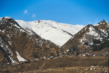 Wall Mural - Early spring. The village is in the mountains. Snow caps on the tops of the mountains. Small village at the foot