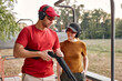 © Roman - Confident male shooting instructor teaches the backslider how to handle weapon on training course in outdoor range. positive teacher and woman in protective spectacles and headset have fun, laugh