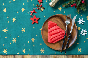 Table setting for Christmas dinner, holiday composition. Table fork and knife set with red paper napkin and fir branch on a rustic celebrate table. Top view flat lay background. Copy space.