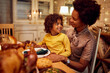 © Drazen - Happy African American mother and daughter talk during Christmas meal at dining table.