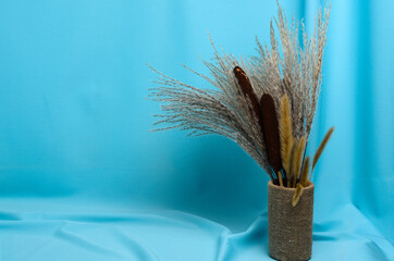 Autumn bouquet of cattails and reeds on a textured background made of soft blue fabric with elegant pleats.