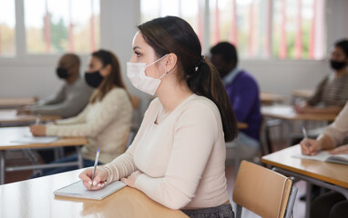 Wall Mural - Young woman in protective face mask listening to lesson in extension school. Concept of necessary precautions and social distancing in coronavirus pandemic..