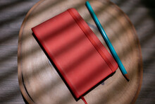 red moleskine with pencil on wooden background for mockup. flat notebook with elastic on shade of blind curtain