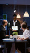© DC Studio - Overworked workaholic businesswoman with dark skin explaining management graphs using tablet overworking in company meeting office room late at night. Multi-ethnic teamwork solving company problem