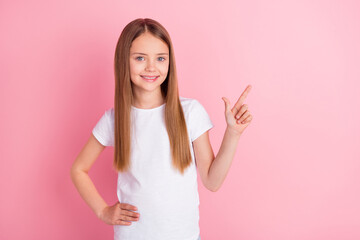 Photo of optimistic blond small girl point empty space wear white t-shirt isolated on pink color background