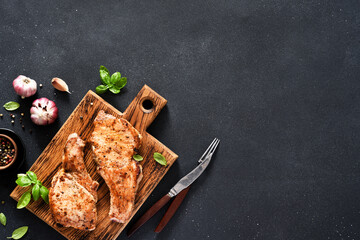 Two grilled pork steaks with garlic and basil on a wooden board on a black background with space for the text. View from above.