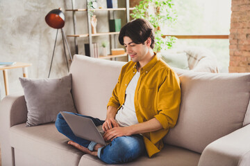 Poster - Photo of positive freelancer programmer guy hold laptop hands typing sit sofa wear yellow shirt home indoors