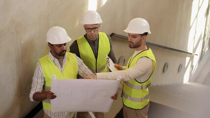 Canvas Print - architecture, construction business and people concept - male architects in helmets discussing blueprint at office