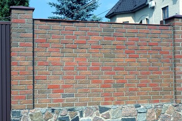 Poster - part of a wall of a fence made of red and brown bricks on a stone foundation in the street