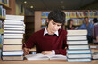 © ER Creative Services - Student writing at desk with stacks of books in library