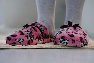 pink domestic slipper with black bow on women's legs, feet on a light plush rug, concept of comfortable shoes for rest, relax and life, taking care of healthy feet, sweet home