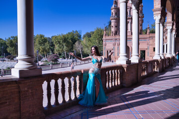 Wall Mural - Middle-aged Hispanic woman, wearing turquoise costume and rhinestones, to dance belly dance, making figures while dancing next to a stone balustrade. Belly dance concept.