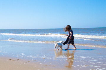 Wall Mural - Young girl playing with a white dog on. Cromer beach in a sunny day of summer, joy, happiness, holiday, vacation in England, United Kingdom, Norfolk coast, North sea
