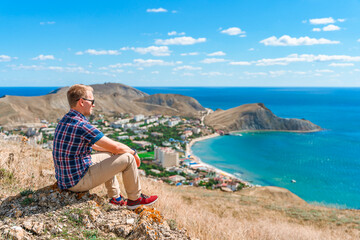 A young man is sitting on a rock on a high mountain overlooking the coast of Ordzhonikidze village in Crimea