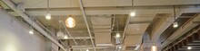 White industrial style ceiling with exposed air conditioner vent grid duct pipes and lamps banner