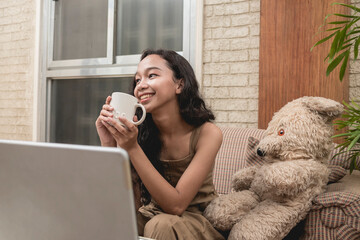 A cheerful and optimistic teenage lady has positive thoughts while enjoying a cup of coffee. Sitting on the couch with her favorite teddy bear in the living room.