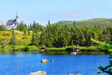 Looking Across A Pond To A Church On Top Of A Hill, Surrounded By Forest.