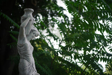 Wall Mural - sculpture of a girl in the spring park. An old statue in a park of a sensual semi-nude Greek or Italian Renaissance woman with a vase in a city park. sunny day in the summer garden. close-up