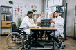 © Sofiia Shunkina - Multiracial male and female doctors sitting together at office desk and discussing results of x ray scan. African american man who using wheelchair having conference meeting with colleagues.