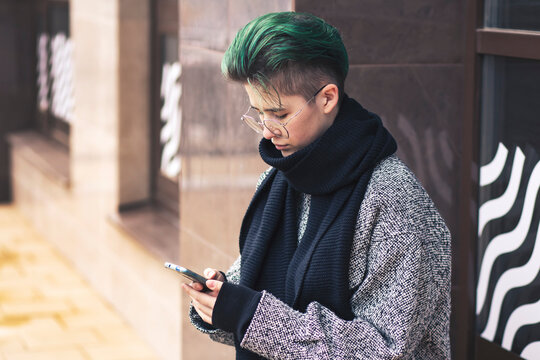 A modern girl in casual clothes uses a smartphone on a city street in autumn. Social networks, communication.